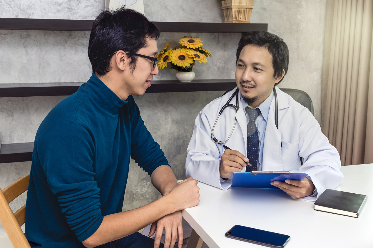 Doctor consulting male patient and writing notes on clipboard at clinic.